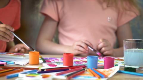 close up of children's hands creating art with brushes and containers of paint