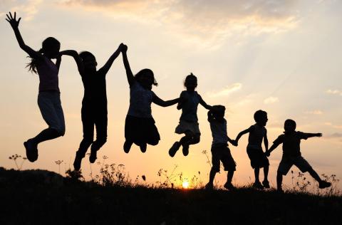 silhouette of kids holding hands and jumping against sunset