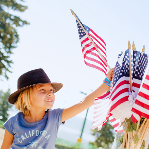 child wearing hat grabbing small American flag out of pile