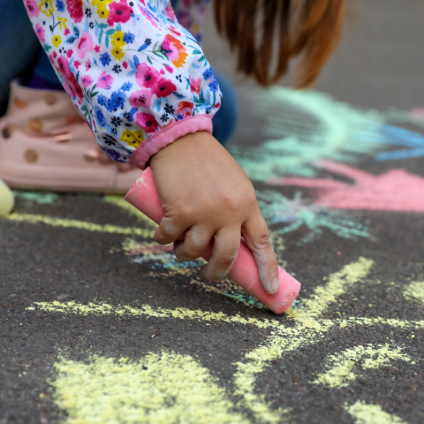 closeup of girl with flowery using pink chalk on sidewalk