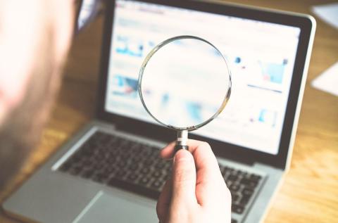 man holding magnifying glass looking at laptop