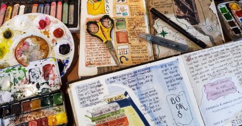 old book with watercolor paints, brushes, scissors and other art items used to decorate the book pages