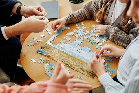 hands of a group of people sitting at a table putting together a jigsaw puzzle