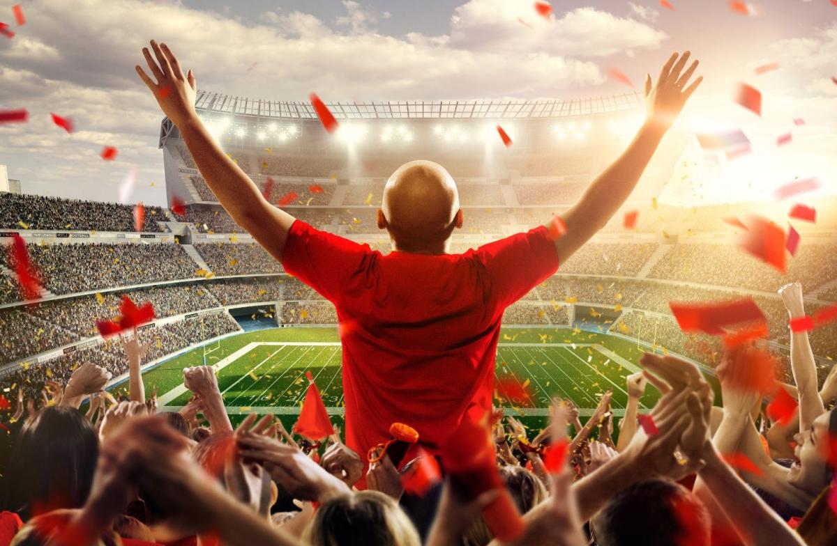 Man standing up and cheering in stands at football stadium with crowd