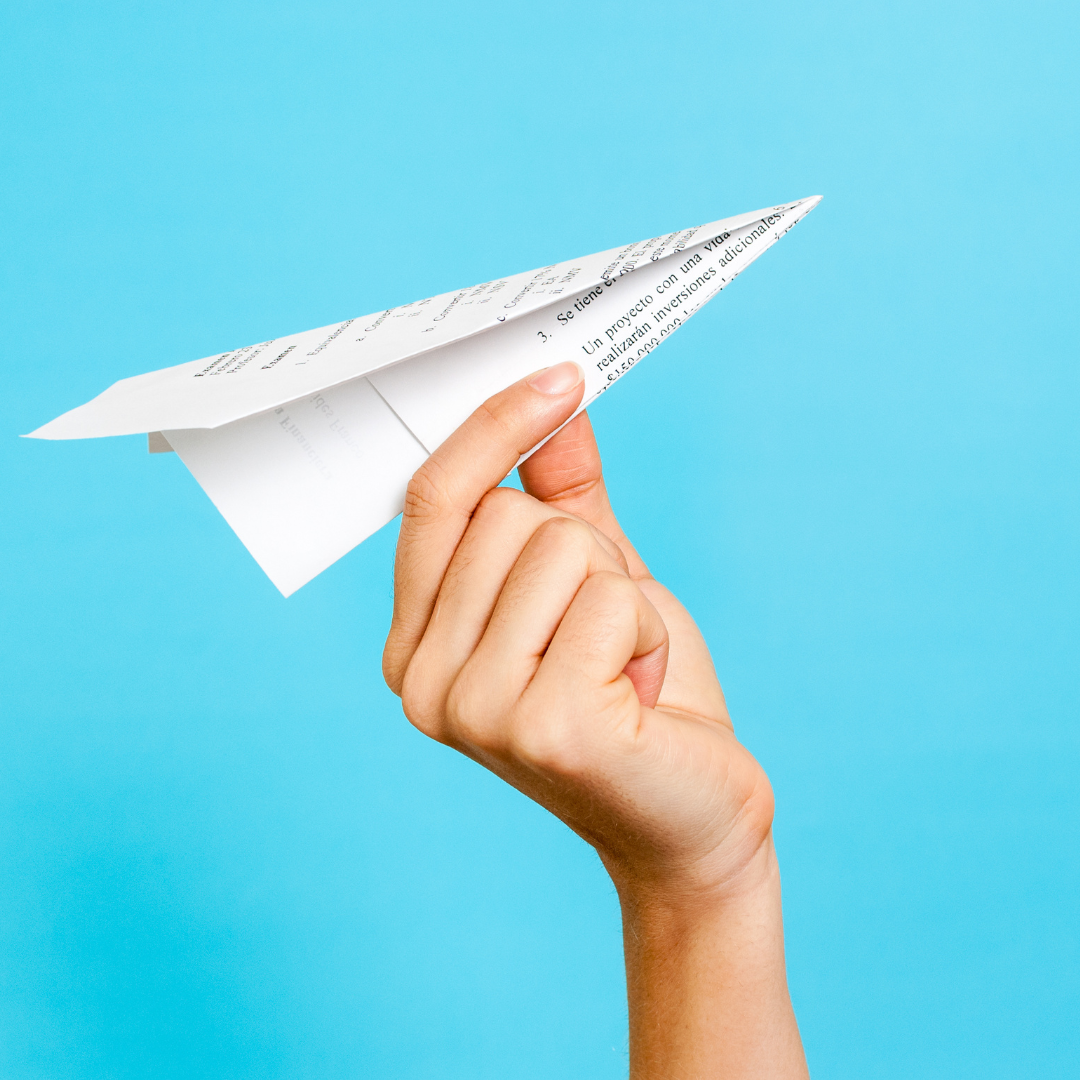 person holding paper airplane against a blue background