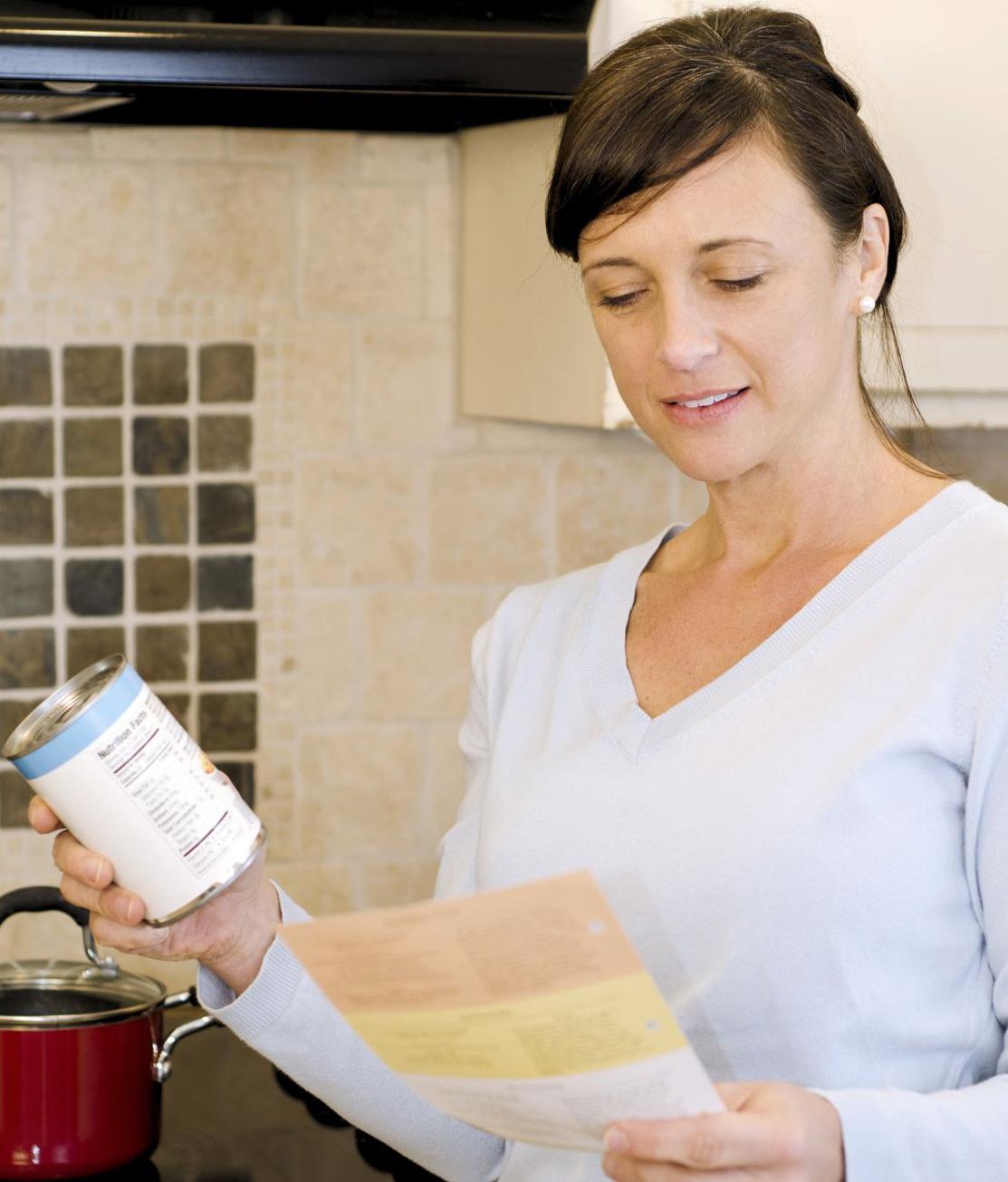 woman holding a can in one hand, while looking at a recipe on a piece of paper in her other hand